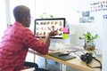 African American man sitting at creative studio desk reviewing thumbnails on computer using tablet Royalty Free Stock Photo