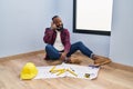 African american man sitting on the floor at new home looking at blueprints smiling doing phone gesture with hand and fingers like Royalty Free Stock Photo