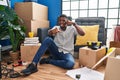 African american man sitting on the floor at new home smiling doing talking on the telephone gesture and pointing to you Royalty Free Stock Photo