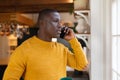 African american man standing in kitchen at home talking on smartphone and looking out of window Royalty Free Stock Photo