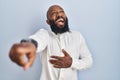 African american man standing over blue background laughing at you, pointing finger to the camera with hand over body, shame Royalty Free Stock Photo