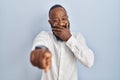 African american man standing over blue background laughing at you, pointing finger to the camera with hand over mouth, shame Royalty Free Stock Photo