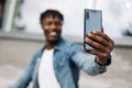 African American man takes a selfie on the street, in front of a glass building, traveling alone, phone close-up Royalty Free Stock Photo