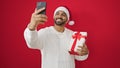 African american man taking a selfie picture holding christmas gift over isolated red background