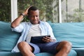 African American man using digital tablet while sitting on cozy sofa couch at home Royalty Free Stock Photo