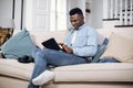 African american man using tablet on comfy couch Royalty Free Stock Photo