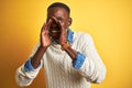 African american man wearing denim shirt and white sweater over isolated yellow background Shouting angry out loud with hands over Royalty Free Stock Photo