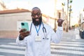 African american man wearing doctor uniform doing video call with smartphone pointing thumb up to the side smiling happy with open Royalty Free Stock Photo
