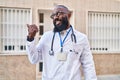 African american man wearing doctor uniform and stethoscope pointing thumb up to the side smiling happy with open mouth Royalty Free Stock Photo