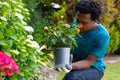 African american man wearing gardening gloves smelling flowers while gardening in the garden