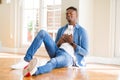 African american man wearing headphones listening to music sitting on the floor smiling with hands on chest with closed eyes and Royalty Free Stock Photo