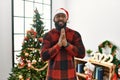 African american man wearing santa claus hat standing by christmas tree begging and praying with hands together with hope Royalty Free Stock Photo