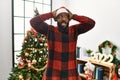 African american man wearing santa claus hat standing by christmas tree crazy and scared with hands on head, afraid and surprised Royalty Free Stock Photo