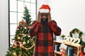 African american man wearing santa claus hat standing by christmas tree with hand on head, headache because stress Royalty Free Stock Photo