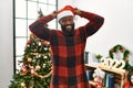 African american man wearing santa claus hat standing by christmas tree posing funny and crazy with fingers on head as bunny ears, Royalty Free Stock Photo