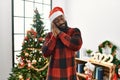 African american man wearing santa claus hat standing by christmas tree sleeping tired dreaming and posing with hands together