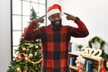 African american man wearing santa claus hat standing by christmas tree smiling pointing to head with both hands finger, great Royalty Free Stock Photo