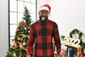 African american man wearing santa claus hat standing by christmas tree sticking tongue out happy with funny expression Royalty Free Stock Photo