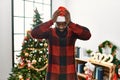 African american man wearing santa claus hat standing by christmas tree suffering from headache desperate and stressed because Royalty Free Stock Photo