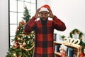 African american man wearing santa claus hat standing by christmas tree trying to open eyes with fingers, sleepy and tired for Royalty Free Stock Photo