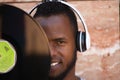 African american man with white headphones holding a vinyl record in his hand and covering part of his face Royalty Free Stock Photo