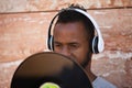 African american man with white headphones holding a vinyl record in his hand and covering part of his face Royalty Free Stock Photo