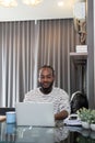 African American man working with laptop computer remote while sitting at glass table in living room. Black guy do Royalty Free Stock Photo