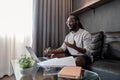 African American man working with laptop computer video calling and conference, remote work while sitting at sofa in Royalty Free Stock Photo