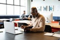 African american mature businessman writing in diary and looking at laptop in creative office Royalty Free Stock Photo