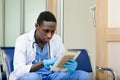 African American medical male doctor wear white coat hanging stethoscope using digital tablet sitting in hospital. Royalty Free Stock Photo