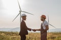 Colleagues shaking hands with wind turbines on background