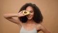 African American model beautiful attractive woman girl in beige ad advertise background holding fresh avocado near face Royalty Free Stock Photo