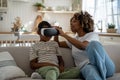 African American modern mom helping little boy son to put on virtual reality headset