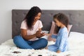 African American mother applying polish on her little daughter& x27;s nails on bed indoors, full length. Family pastimes Royalty Free Stock Photo