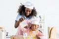 african american mother and daughter in chef hats pouring milk in bowl with ingredientes