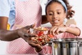 african american mother and daughter putting ingredientes in saucepan