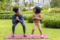 African American mother and her daughter in sport yoga suit are doing squat exercise outdoor in the park near their apartment for