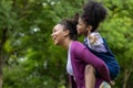 African American mother is playing piggyback riding with her young daughter while having a summer picnic in the public park for Royalty Free Stock Photo