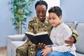 African american mother and son wearing soldier uniform reading book at home Royalty Free Stock Photo