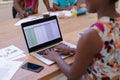 African american mother working at home using laptop with son and daughter in background