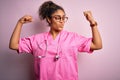 African american nurse girl wearing medical uniform and stethoscope over pink background showing arms muscles smiling proud Royalty Free Stock Photo