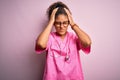 African american nurse girl wearing medical uniform and stethoscope over pink background suffering from headache desperate and