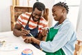 African american painter couple smiling happy painting hands sitting on the table at art studio