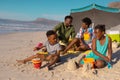 African american parents sitting under umbrella while children playing with sand, pails and shovels Royalty Free Stock Photo