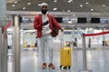 Black tourist man waiting to check in in airport terminal, stands with suitcase, using smartphone. Royalty Free Stock Photo