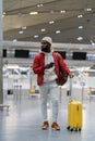 Black tourist man waiting to check in in airport terminal, stands with suitcase, using smartphone. Royalty Free Stock Photo