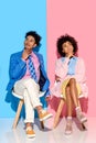 african american pensive couple sitting on chairs against pink and blue