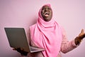 African american plus size woman wearing muslim hijab using laptop over pink background crazy and mad shouting and yelling with Royalty Free Stock Photo