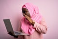 African american plus size woman wearing muslim hijab using laptop over pink background shouting and screaming loud to side with Royalty Free Stock Photo