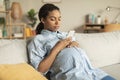African american pregnant woman using smartphone, sitting on couch at home, surfing internet or texting with doctor Royalty Free Stock Photo